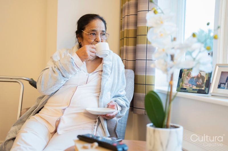 Senior lady drinking coffee and looking through window in bedroom at nursing home