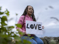 Portrait of teenage girl sitting on stone wall holding peace sign