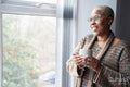 Mature woman with coffee cup looking through window