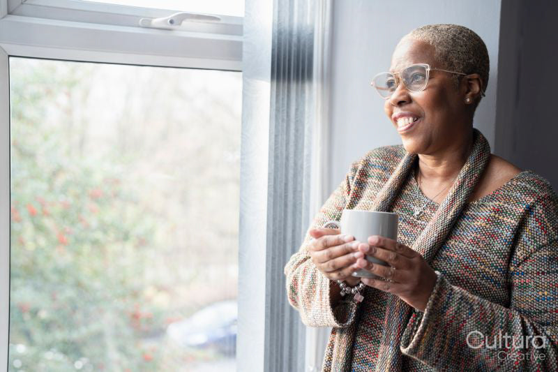 Mature woman with coffee cup looking through window