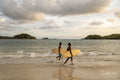 Indonesia, Lombok, Surfers walking on beach at sunset