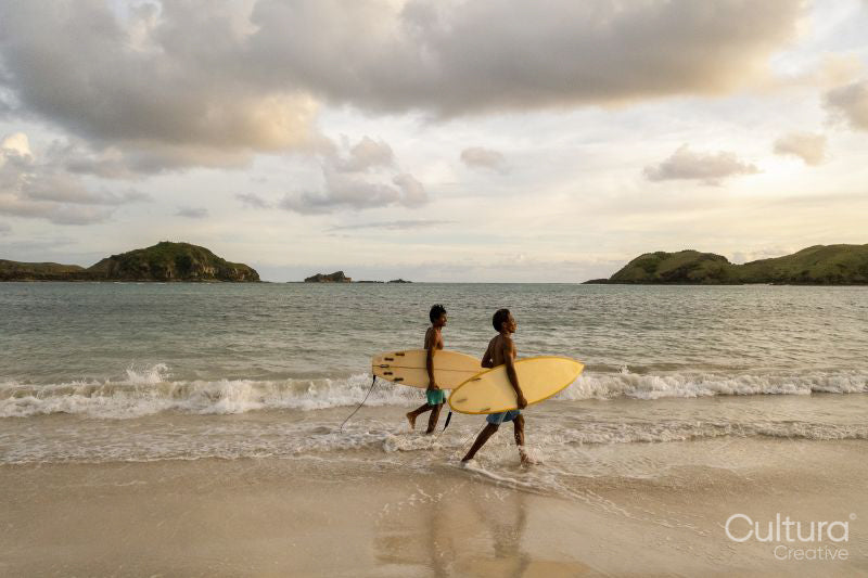 Indonesia, Lombok, Surfers walking on beach at sunset