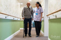 Care giver assisting senior man while walking along corridor in nursing home