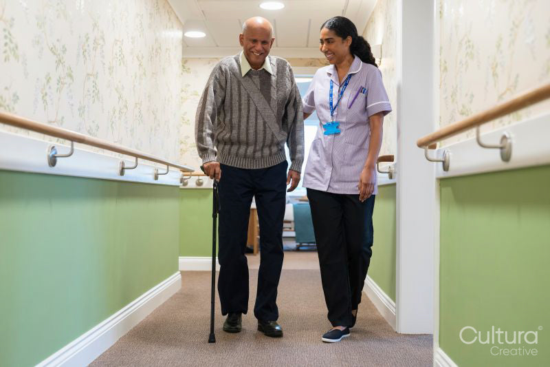 Care giver assisting senior man while walking along corridor in nursing home