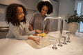 Smiling mother assisting daughter washing dishes in kitchen