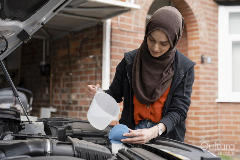 Woman wearing hijab filling water tank in car engine
