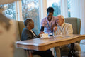 Smiling senior people and nurse talking at table in nursing home