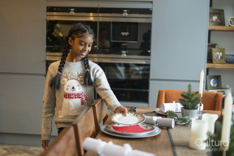 Smiling girl arranging plates on table for Christmas dinner