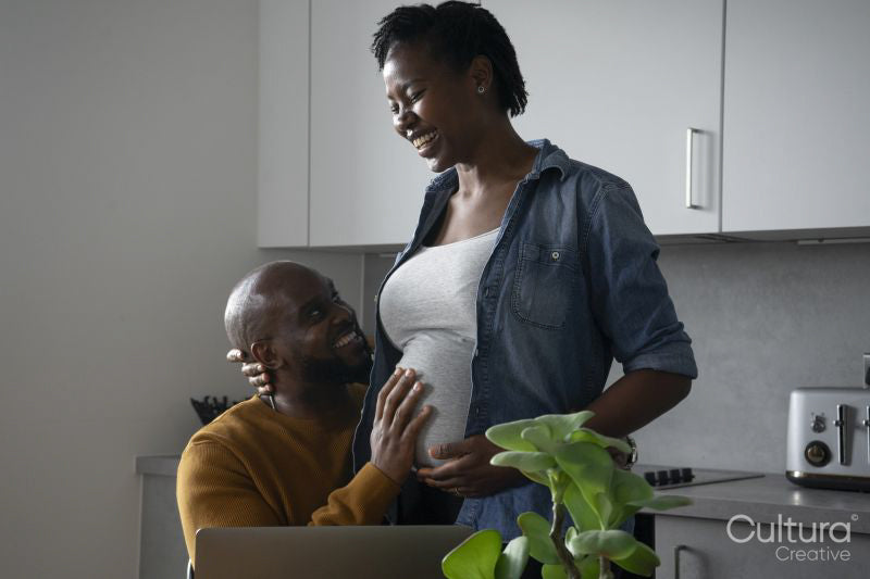 Smiling man touching pregnant woman's belly in kitchen