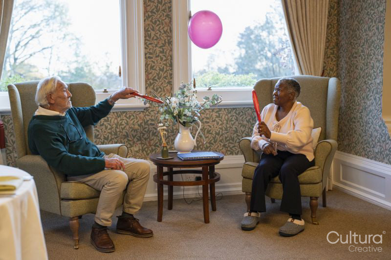 Smiling senior man and woman playing with balloon in nursing home