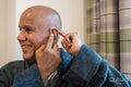 Senior man putting on hearing aid in his room at nursing home