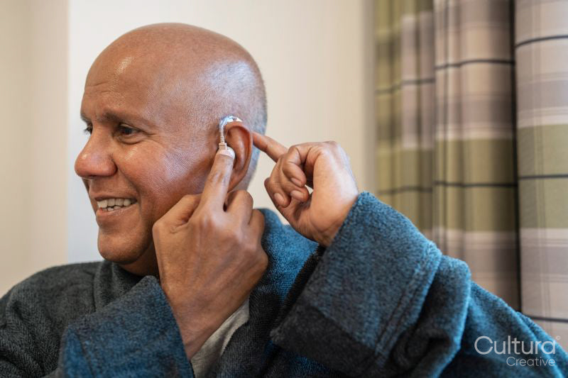 Senior man putting on hearing aid in his room at nursing home