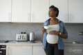Pregnant woman holding tea cup in kitchen