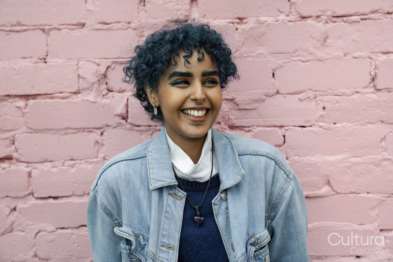 Smiling young woman standing against pink wall