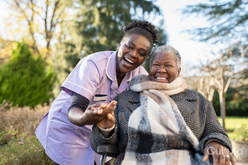 Smiling nurse and senior woman in wheelchair going on walk in park