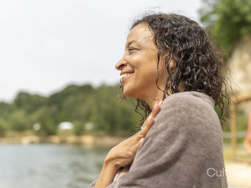 Portrait of smiling woman wrapped in towel by lake