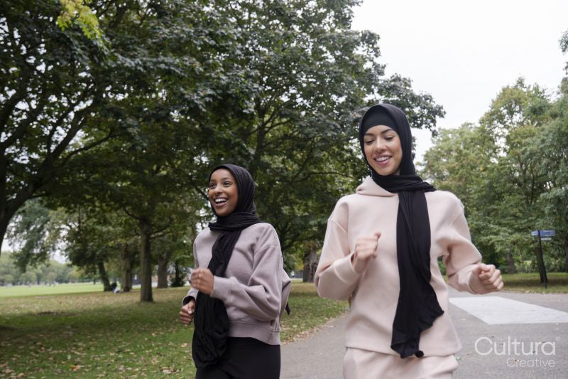 Two smiling women in hijabs jogging in park