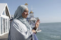 Portrait of thoughtful Muslim woman looking at sea and waving on sunny day