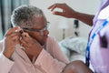 Caregiver assisting senior woman adjusting hearing aid
