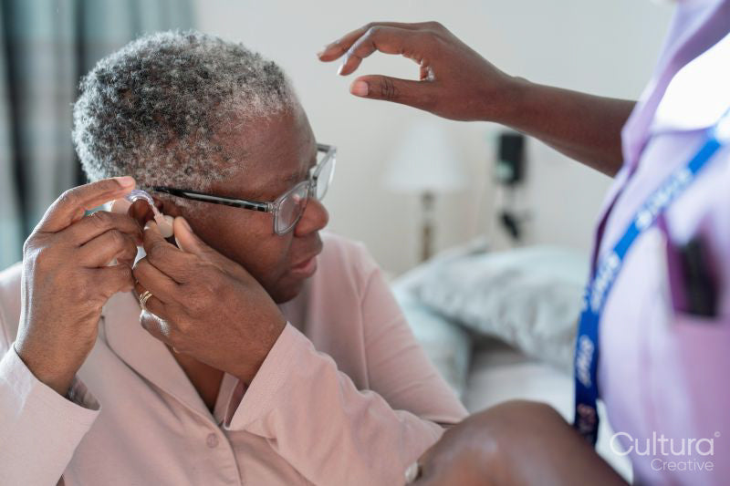 Caregiver assisting senior woman adjusting hearing aid