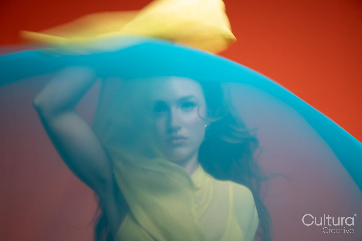 Woman in a yellow dress veiled by flowing blue fabric