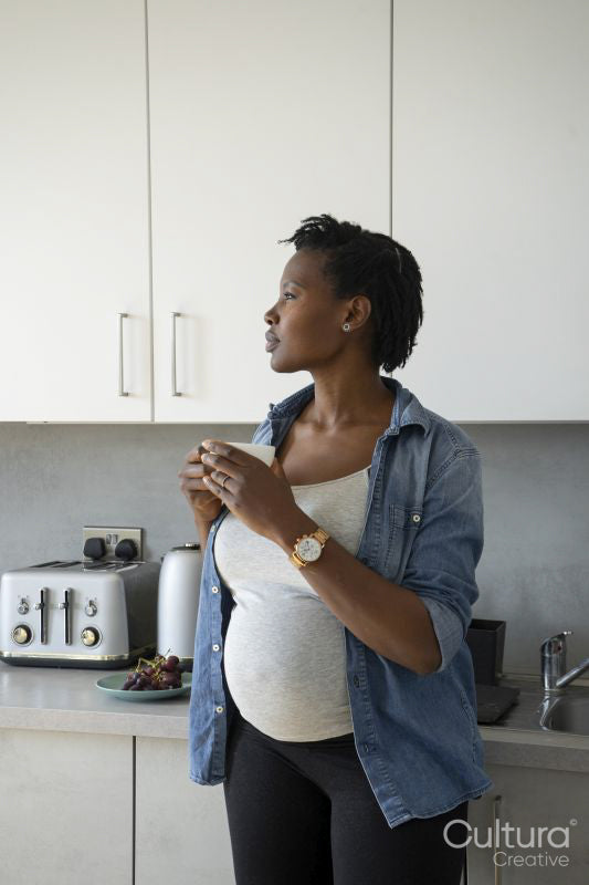 Pregnant woman holding tea cup in kitchen