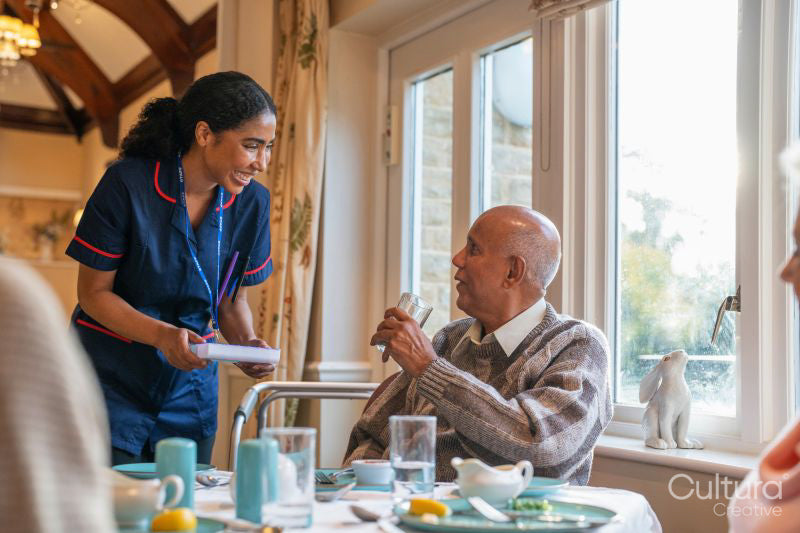 Nurse talking with senior man during dinner at cafeteria in nursing home