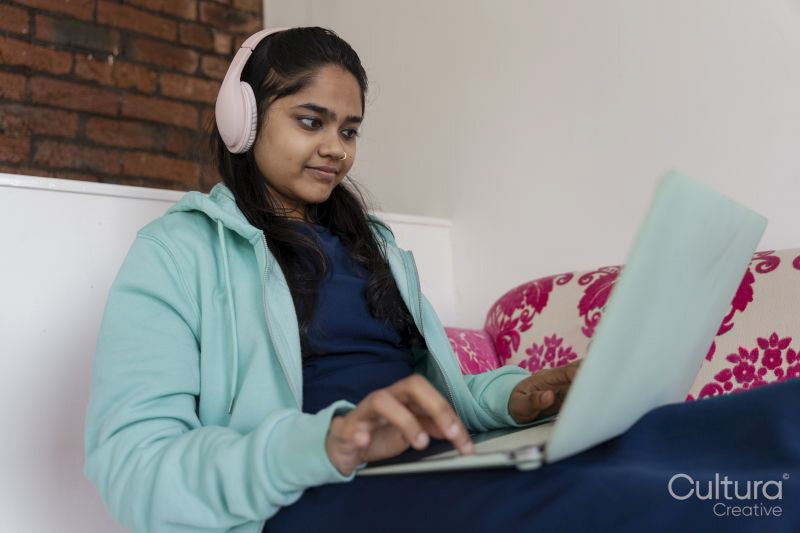 Young female student using laptop and listening to music