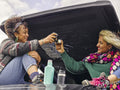 Women sitting on roof of car drinking from insulated drink containers
