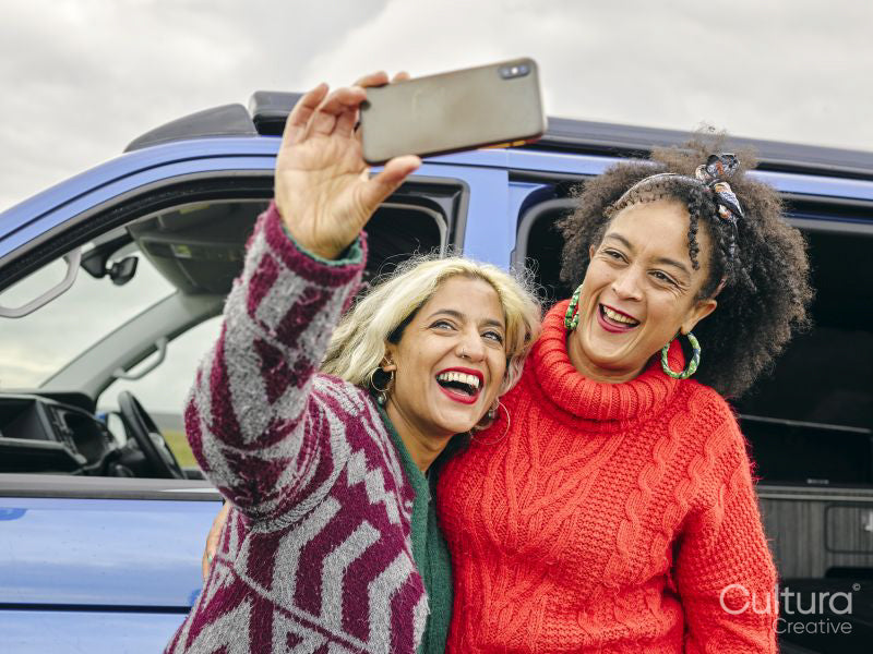 Female couple taking selfie in front of van