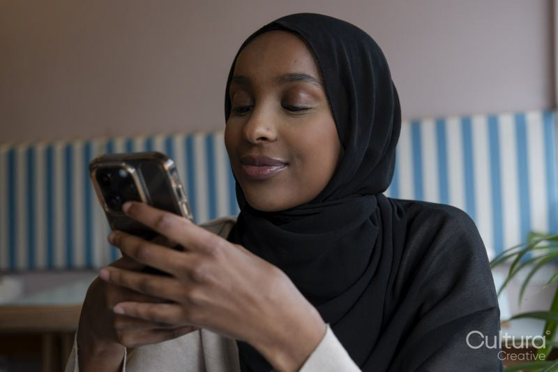 Smiling young woman in hijab using phone in cafe