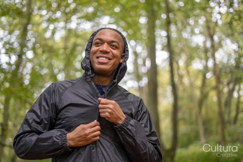 Smiling man zipping up rain jacket in forest
