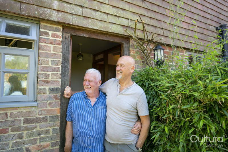 Smiling senior male couple standing in front of house