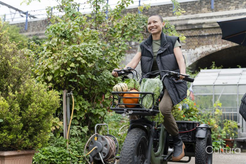 Smiling woman riding cargo electric trike loaded with homegrown vegetables
