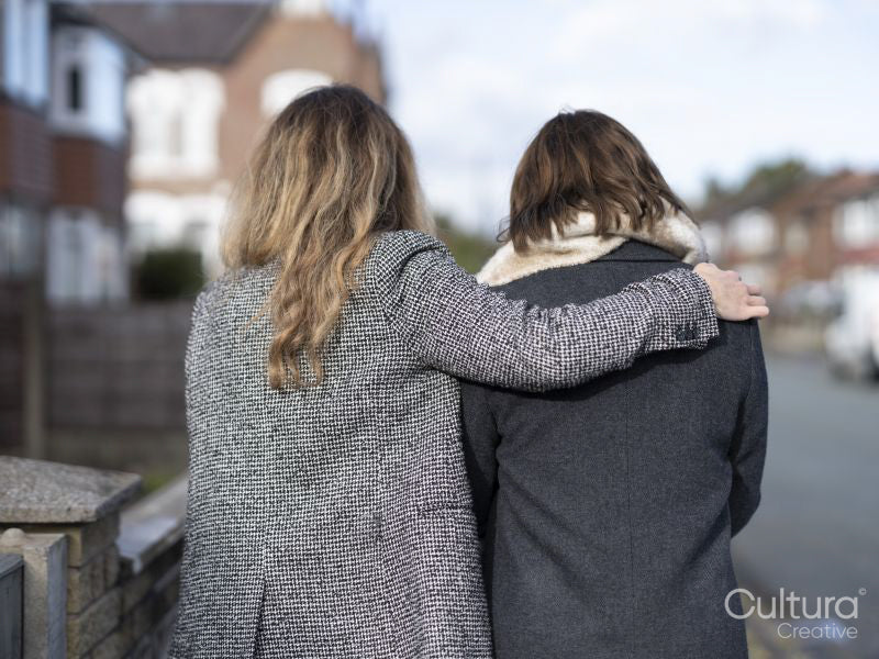 Back view of woman embracing friend and walking together