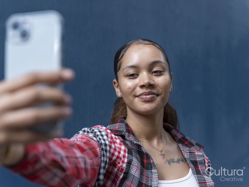 Young woman taking selfie against blue wall