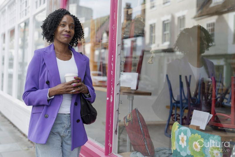 Smiling woman walking with disposable cup on sidewalk