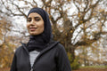 Portrait of smiling woman in black sports clothing and hijab in park