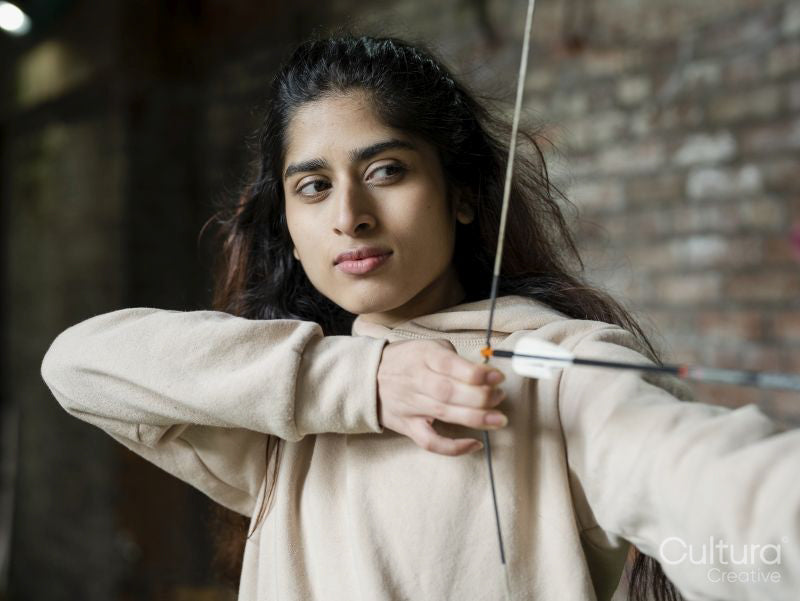 Young brunette female aiming during archery training