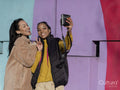 Two young women taking selfies by colorful graffiti wall