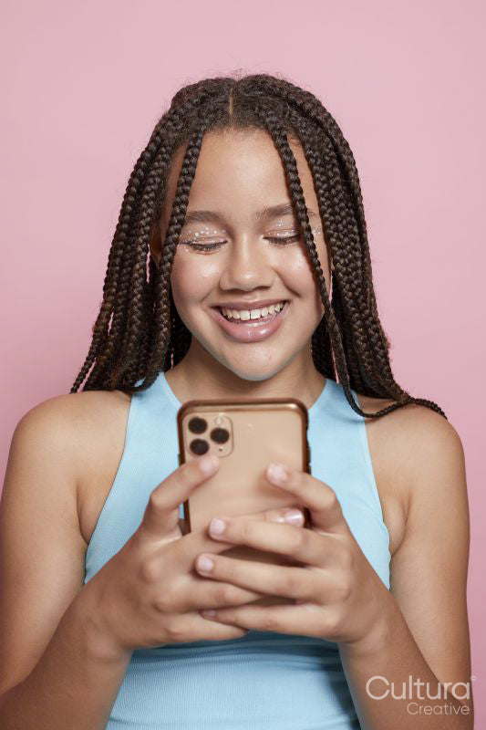 Studio shot of smiling girl with braids looking at smart phone
