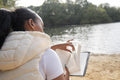 Rear view of woman reading book on lakeshore