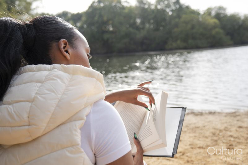 Rear view of woman reading book on lakeshore