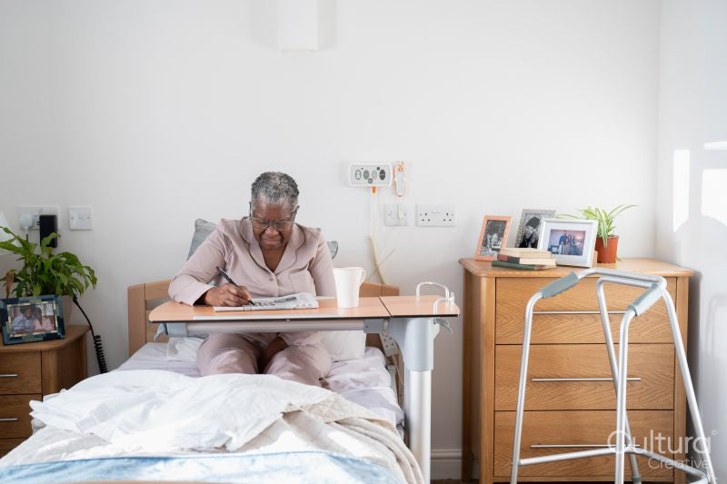 Senior woman in bathrobe sitting on bed and doing crossword puzzle in nursing home