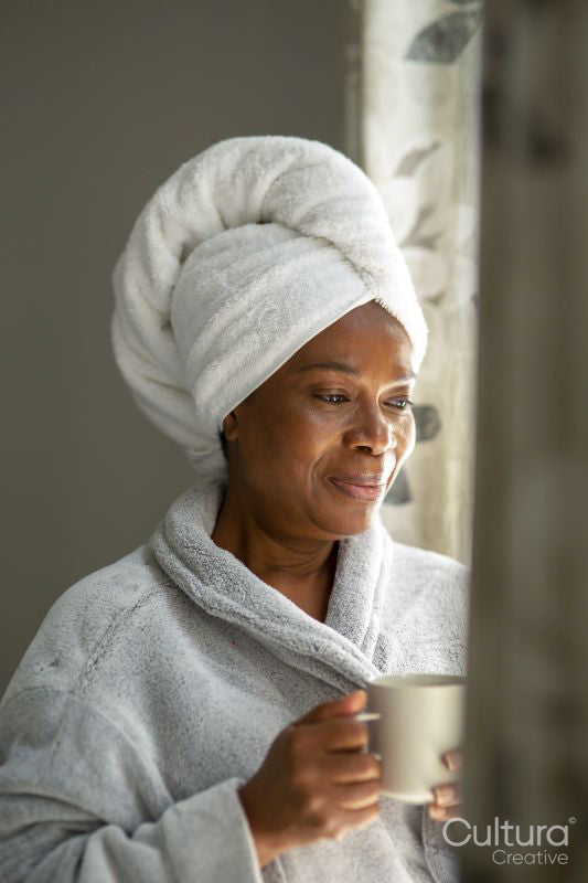Smiling woman in bathrobe and towel on head looking through window