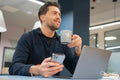 Businessman using phone and laptop in modern office