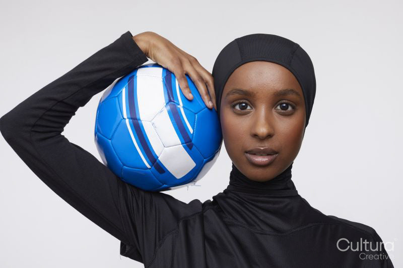 Studio portrait of young woman in hijab holding soccer ball