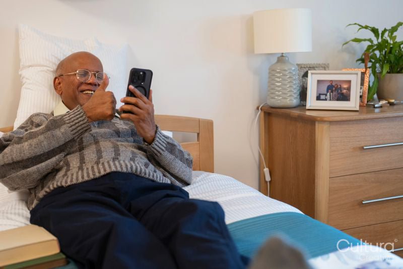 Senior man during video call on phone while lying on bed in his room at nursing home