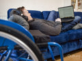Man with headphones and laptop relaxing on sofa next to wheelchair