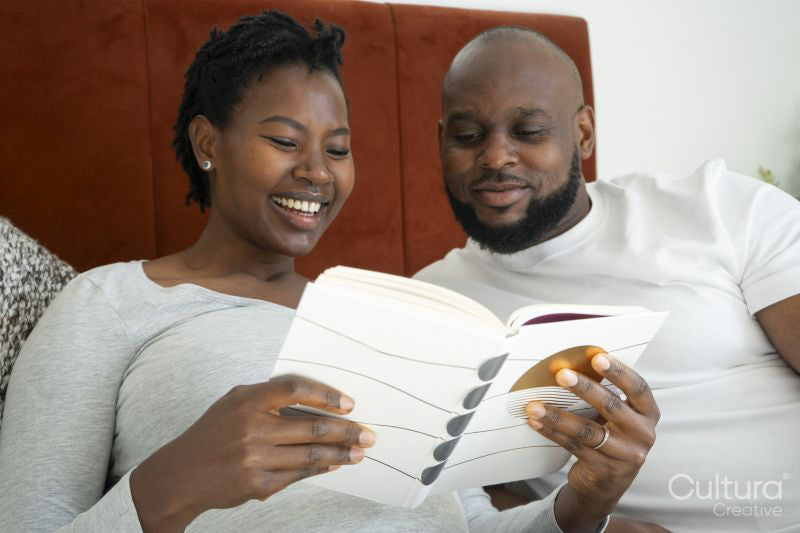 Smiling pregnant woman and man reading book in bed